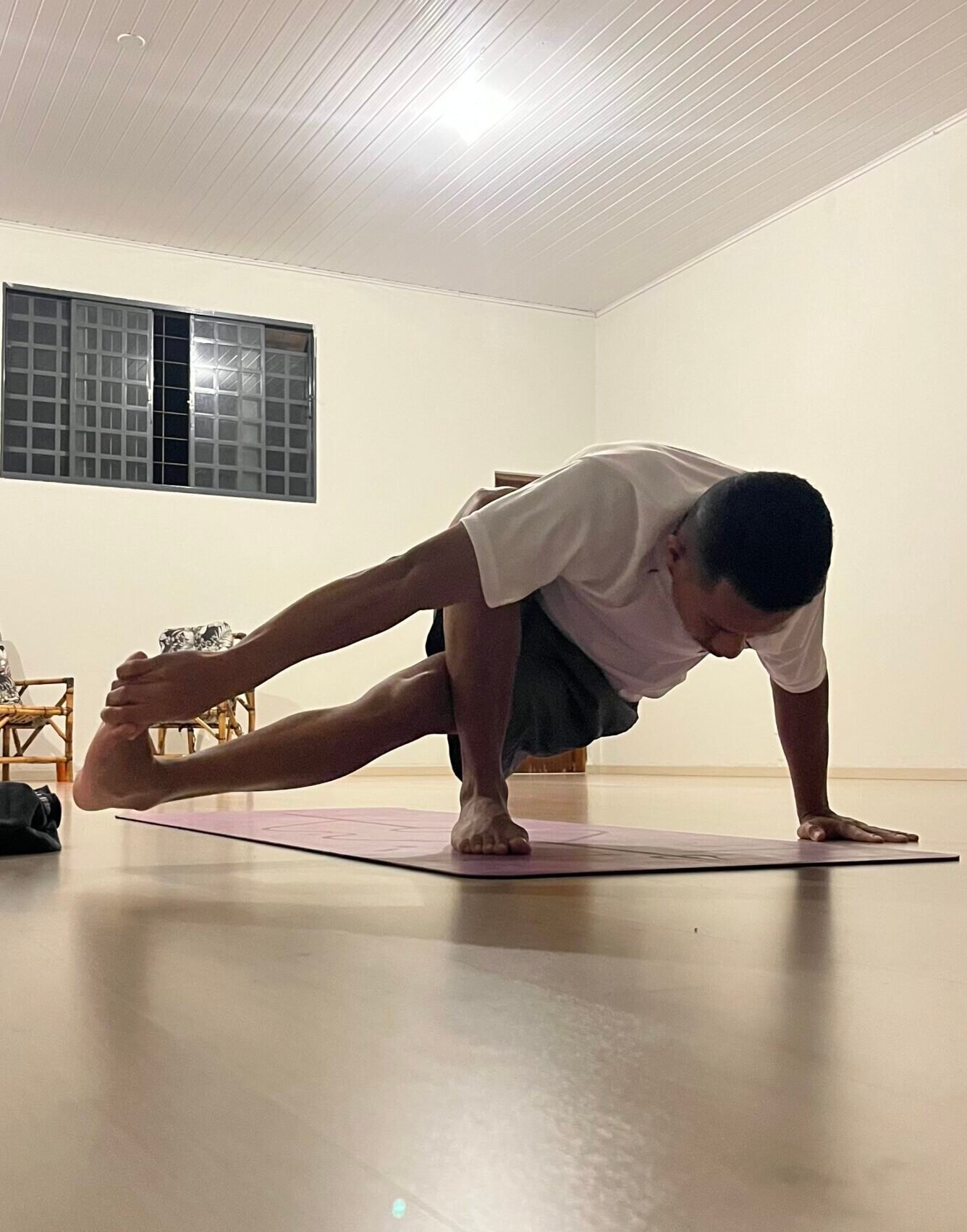Homem praticando yoga em um estúdio em Cianorte-PR, executando a postura de equilíbrio de braço Astavakrasana (postura dos oito ângulos).