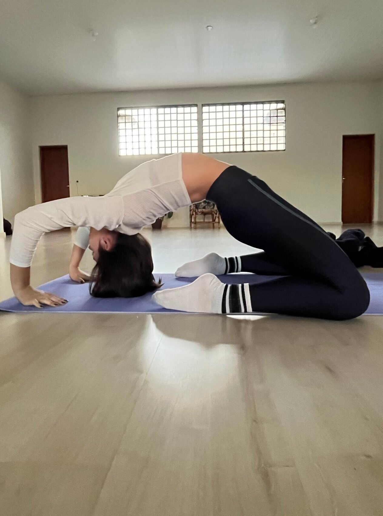 Mulher em um estúdio de yoga em Cianorte-PR executando uma variação avançada da postura do camelo, com um arco profundo nas costas.