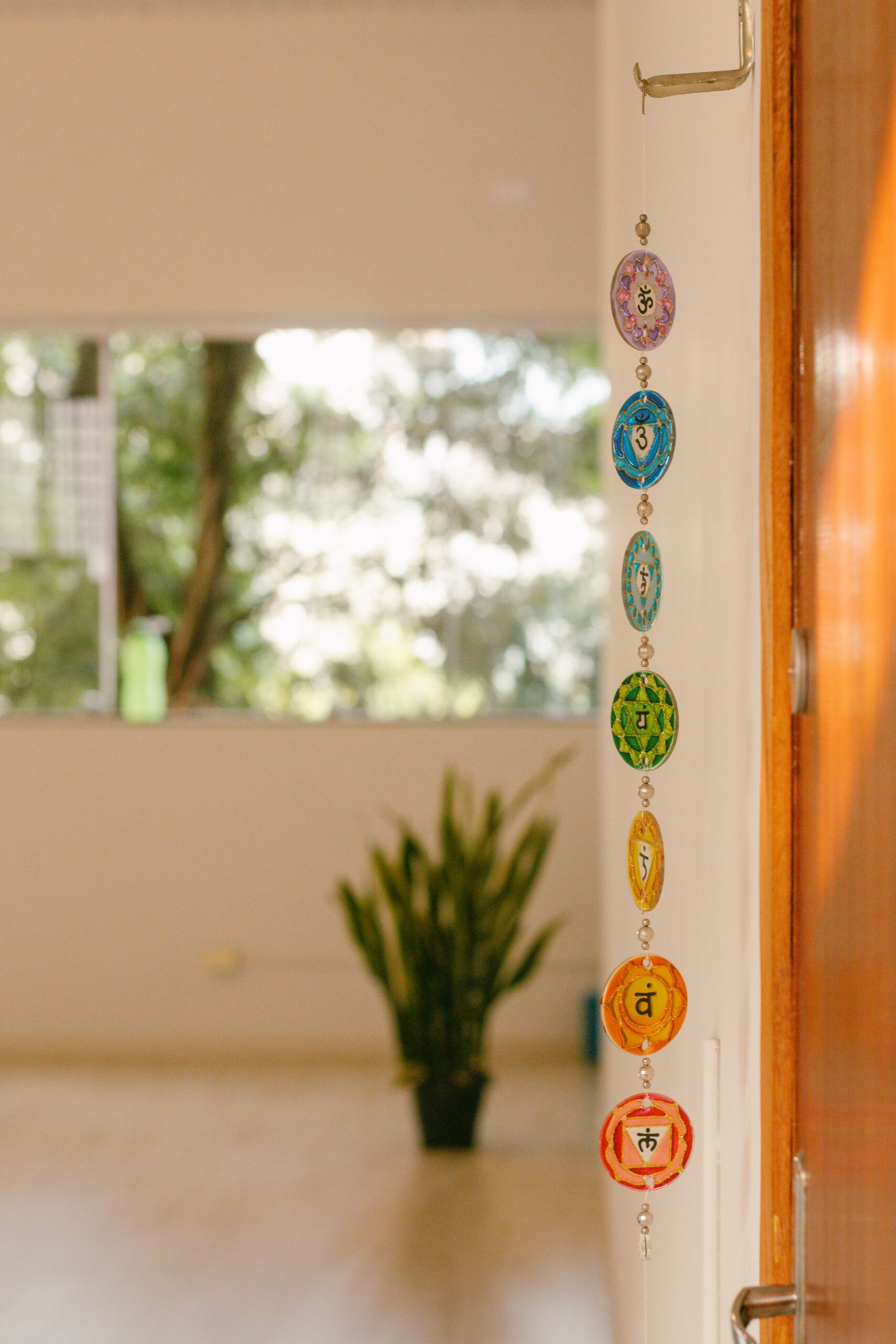 Móbile decorativo com os símbolos dos sete chakras pendurado na entrada do Become - Yoga Studio em Cianorte, com o interior do estúdio ao fundo.